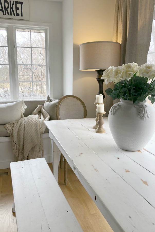 Hello Lovely's white farmhouse table in kitchen with window seat.